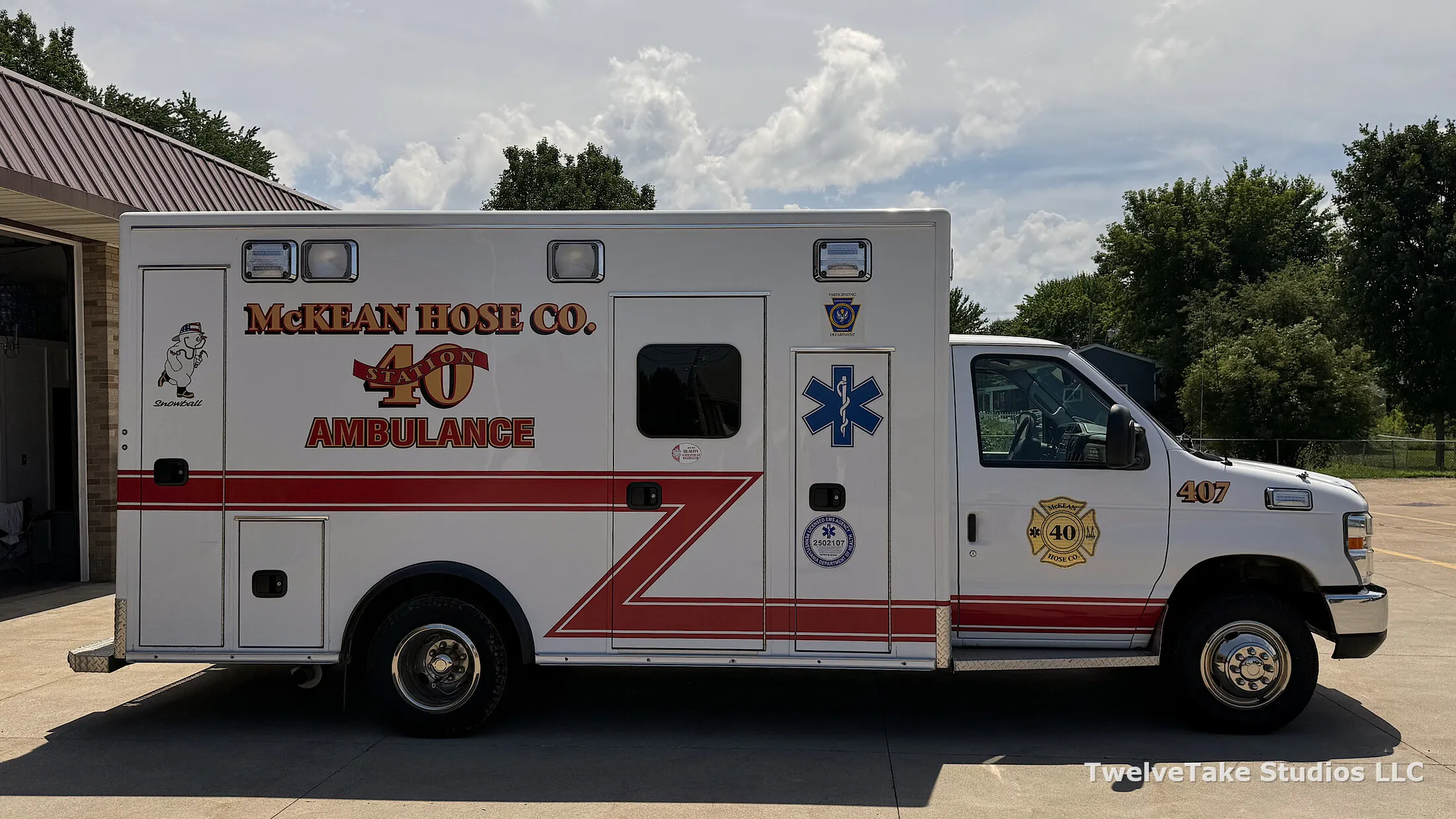Full side view of Ambulance 407 with the blue Star of Life on the side door of the patient compartment and the red chevron stripe running along the box.