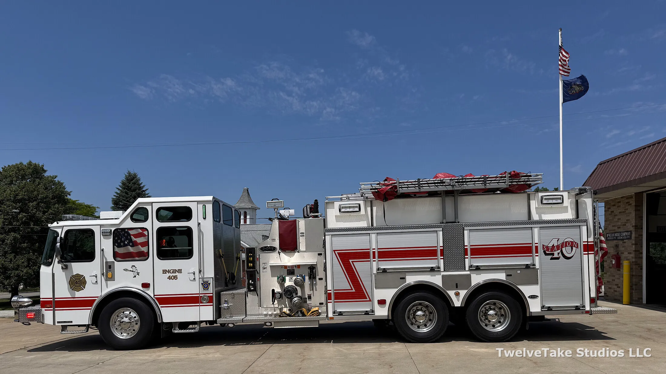 Engine 405 parked on the pavement beside the McKean station, driver's side view, with the American and Pennsylvania flags flying behind it