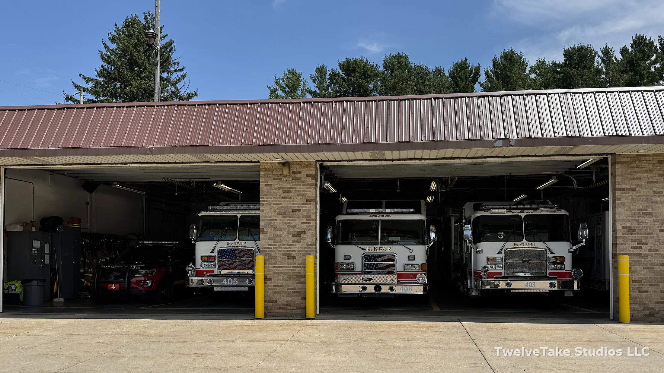 Open truck bays at the McKean Hose Company station with Engine 405, Rescue 408 and Engine 403 parked inside, and a red command vehicle in the left bay
