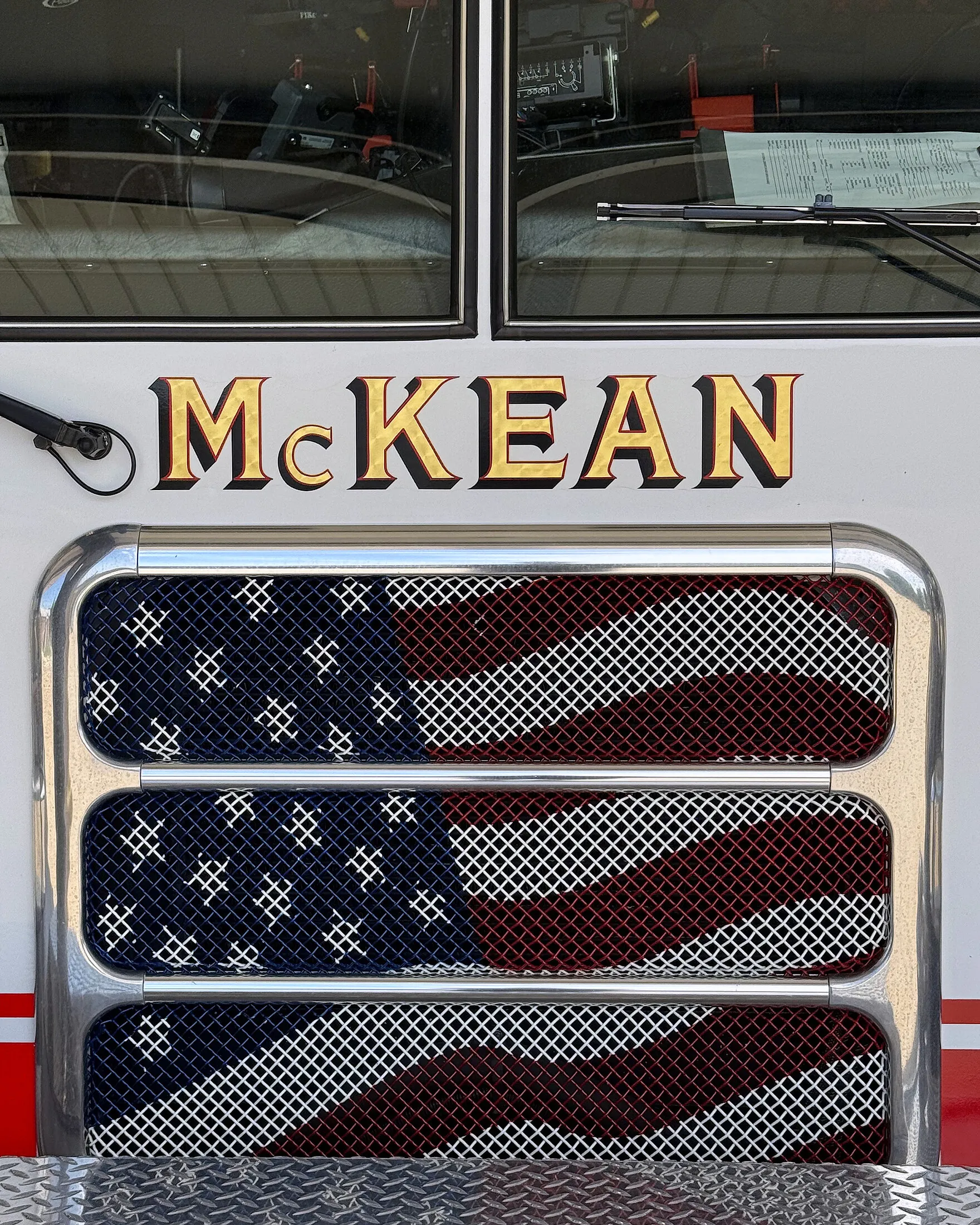 Gold McKEAN lettering on the white cab of a McKean Hose Company engine, above chrome-trimmed intake screens printed with an American flag