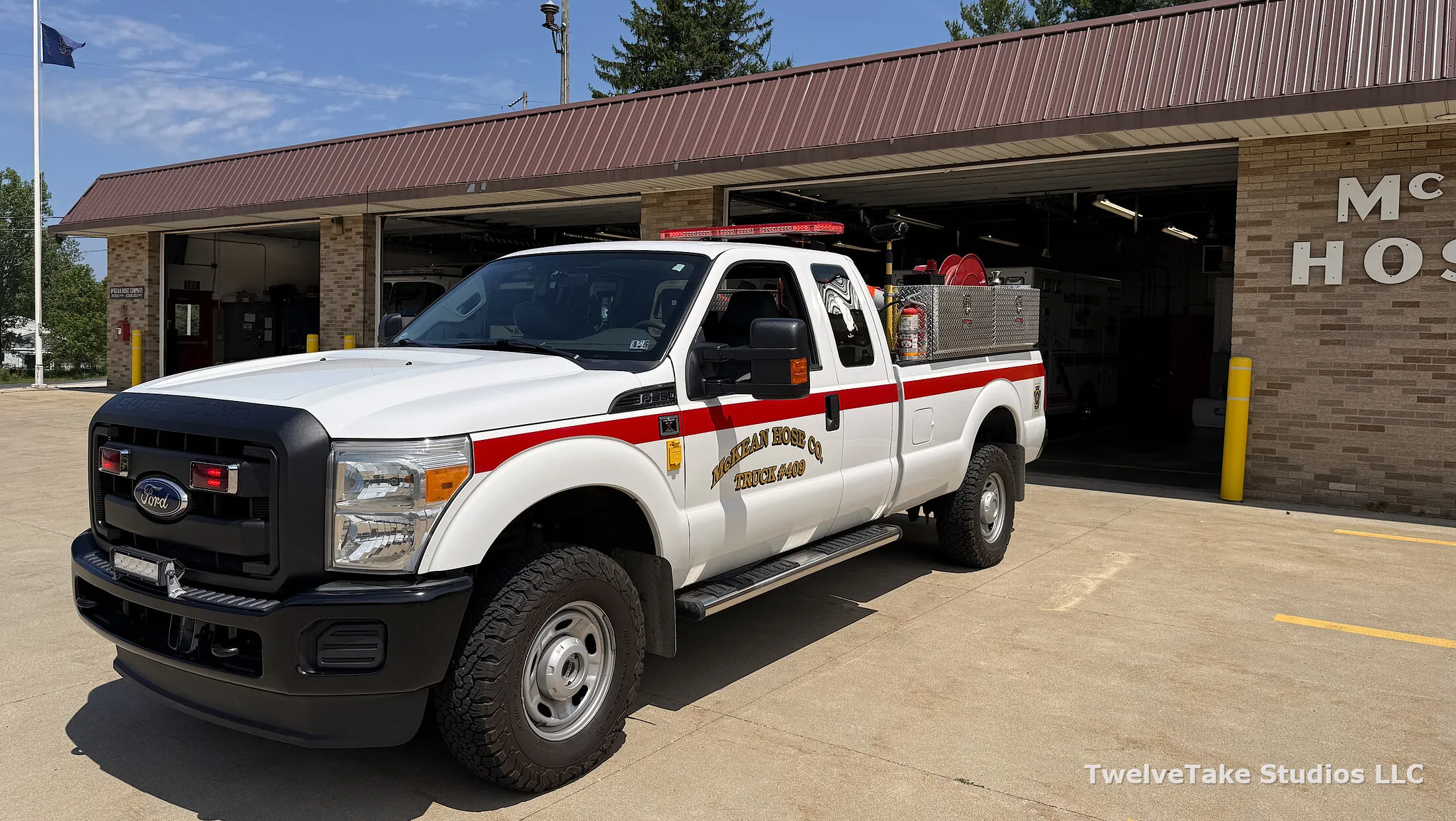 Truck 409, a white Ford Super Duty pickup, angled on the pavement in front of the open bay doors with McKEAN HOSE CO. TRUCK #409 lettered in gold on the cab door and diamond-plate toolboxes in the bed.
