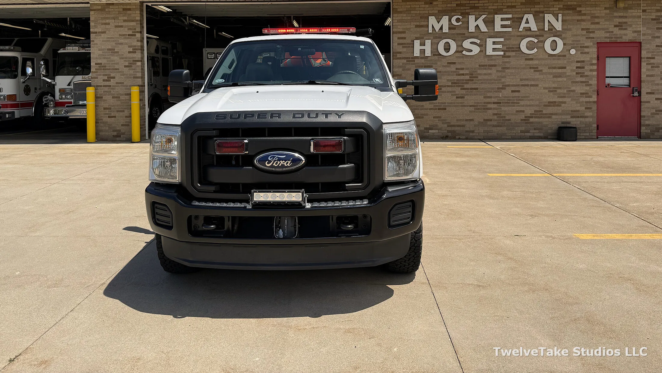 Truck 409 head-on outside the station, warning bar lit across the cab roof, with the raised McKEAN HOSE CO. lettering on the brick wall behind it.